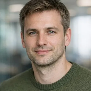 Man in late 30s, dark-blonde hair, grey-green eyes, olive knit sweater, calm expression
